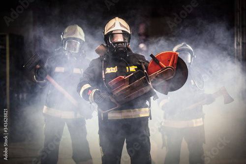 Fotografie Group of professional firefighters wearing full equipment, oxygen masks, and emergency rescue tools, circular hydraulic and gas saw, axe, and sledge hammer