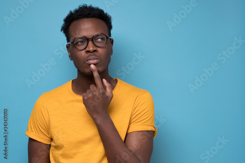 Fototapeta Young african american man, student with finger in mouth in deep thought