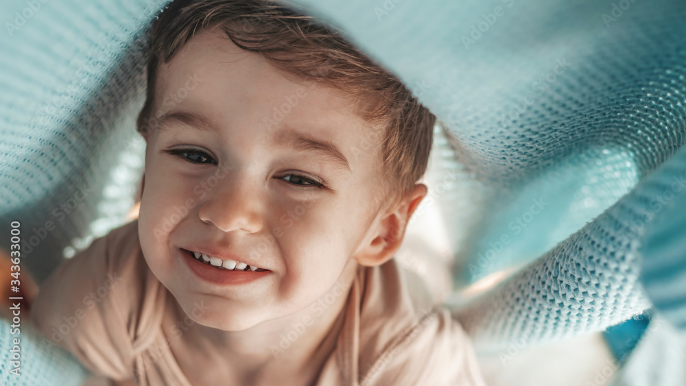Smiling little boy hiding under blanket in bed. Sweet little boy