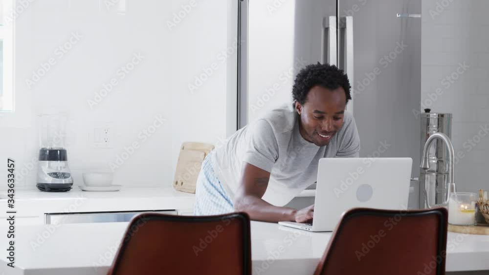 Couple Wearing Pyjamas Standing In Kitchen Working From Home On Laptop Couple Wearing Pyjamas Standing In Kitchen Working From Home On Laptop