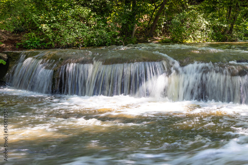 Water cascading over rocks in a woodland stream  sunlight and shade with heavy foliage  horizontal aspect