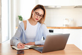 Woman working on laptop at home on kitchen. writing on notepad. Business woman thinking about something important. Woman trying to find a job.
