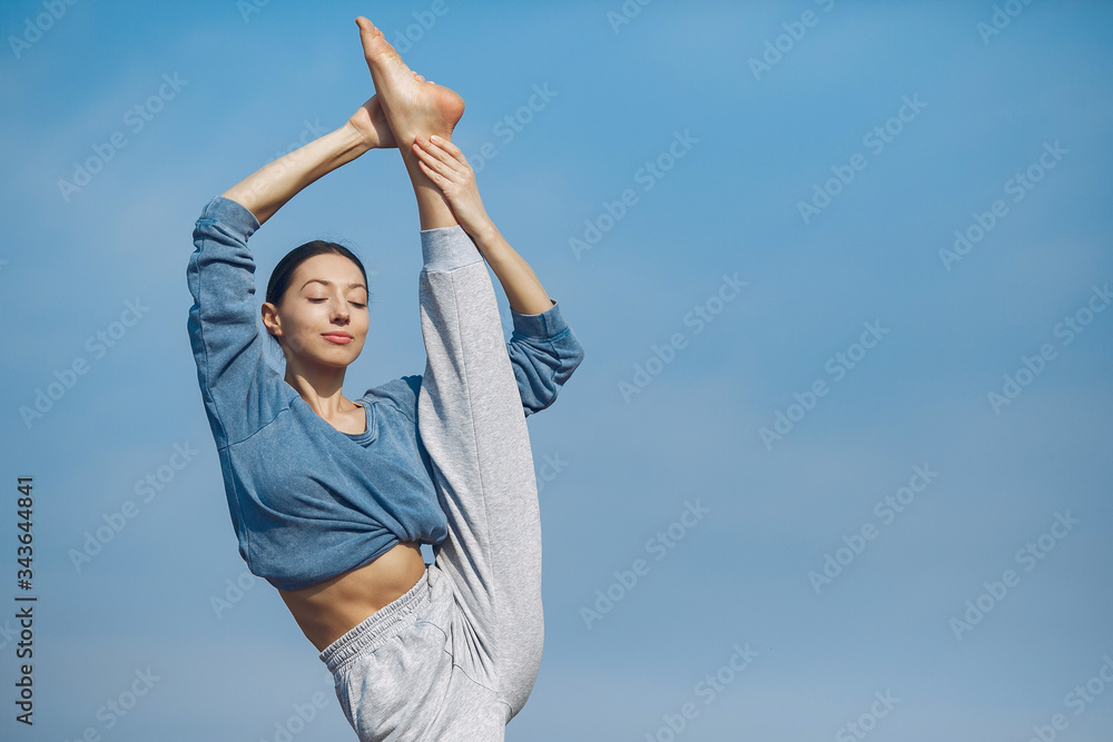 Beautiful girl training on a sky background. Woman in a blue sweater. Lady make a yoga Beautiful girl training on a sky background. Woman in a blue sweater. Lady make a yoga
