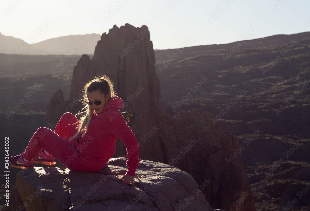 woman in pink tracksuit sitting on a rock watching the views of volcano teide