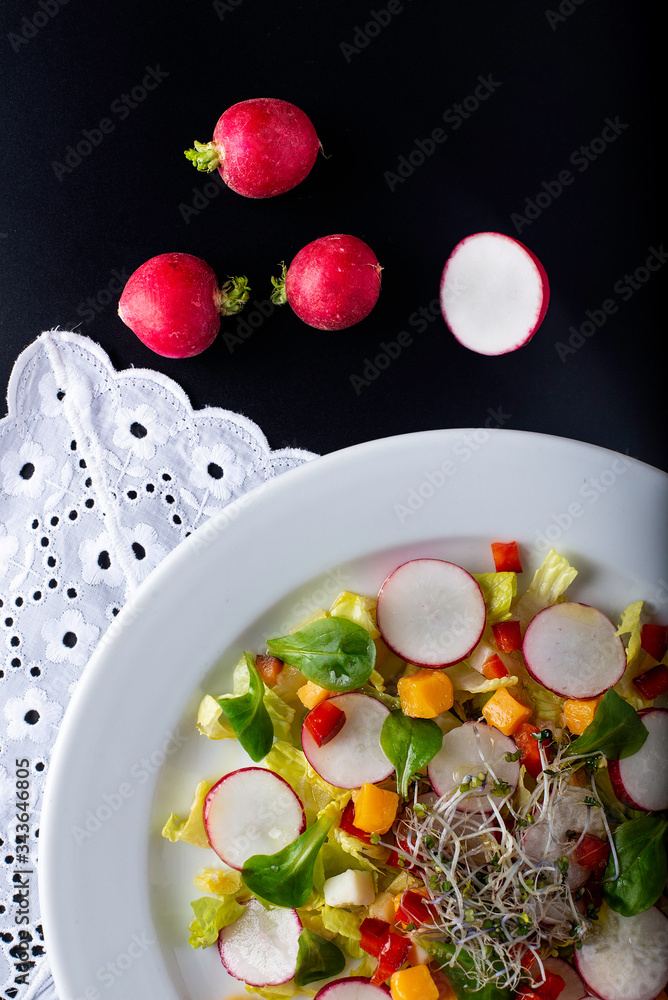 close-up of a mixed salad with pepper cheese, lettuce, radishes and bean sprouts, on a black background close-up of a mixed salad with pepper cheese, lettuce, radishes and bean sprouts, on a black background