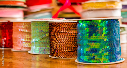 Cose up of shiny rolls of colorful sequins tape, multi-colored over a wooden table in a blurred background photo