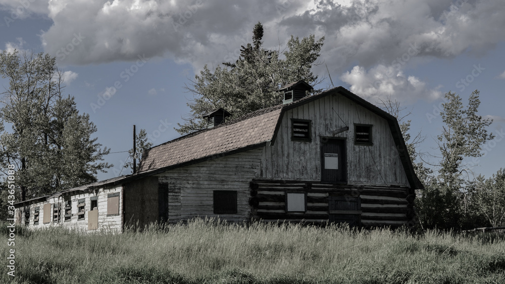 Old abandoned barn on farmland in rural prairies. Rotting wooden barn structure in an overgrown field. Boarded up farm house Old abandoned barn on farmland in rural prairies. Rotting wooden barn structure in an overgrown field. Boarded up farm house