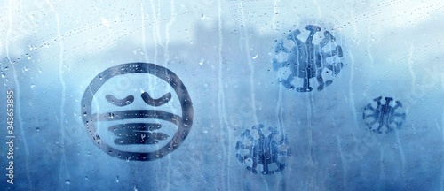 sad face with closed eyes in protective medical mask and three coronavirus molecules figure is painted on wet blue window with raindrops concept photo self-isolation, banner, covid - 19