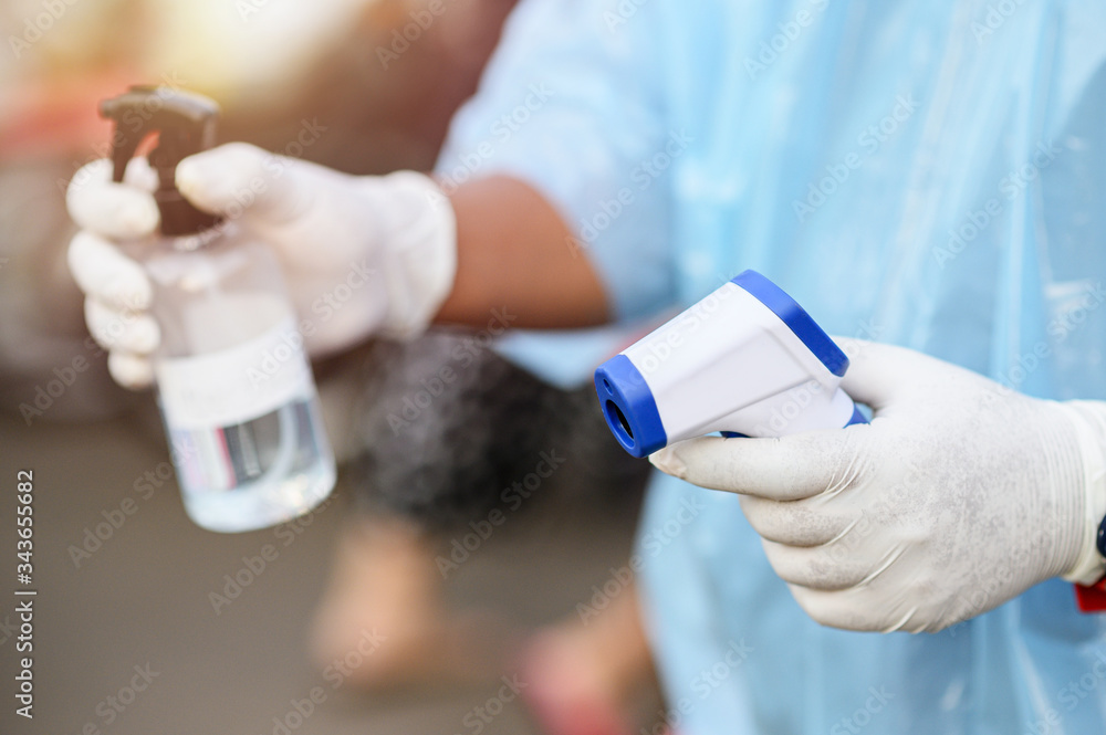 Hold the device a Thermometer and blurred alcohol spray bottle. Hold the device a Thermometer and blurred alcohol spray bottle.