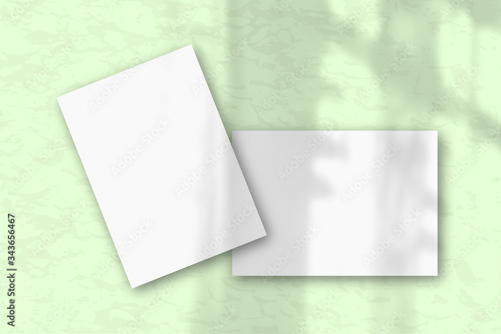 2 sheets of white textured paper against a gray wall. Mockup with an overlay of plant shadow Natural light casts shadows from the window. Flat lay, top view 2 sheets of white textured paper against a gray wall. Mockup with an overlay of plant shadow Natural light casts shadows from the window. Flat lay, top view