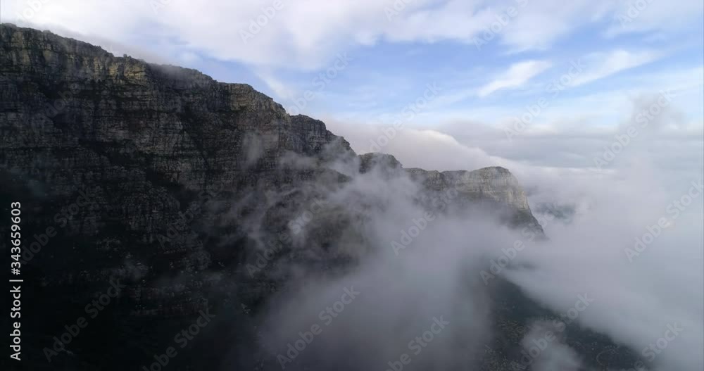 Aerial shot of an amazing mountain among clouds under blue sky, drone flying backwards - Cape Town, South Africa Aerial shot of an amazing mountain among clouds under blue sky, drone flying backwards - Cape Town, South Africa