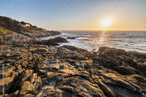 An amazing view of the sunset over the water in the Chilean coast. An idyllic beach scenery with the sunlight illuminating the rocks with orange tones and the sea in the background under a moody sky 