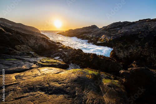 An amazing view of the sunset over the water in the Chilean coast. An idyllic beach scenery with the sunlight illuminating the rocks with orange tones and the sea in the background under a moody sky 