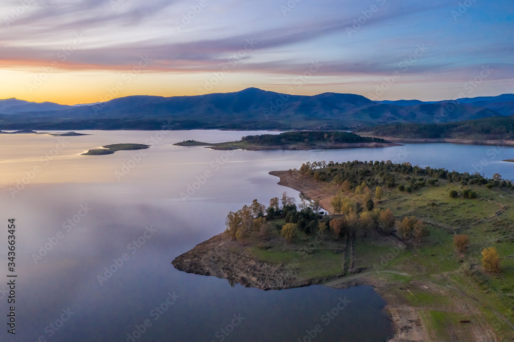 Aerial view of Gabriel y Galan lake at Extremadura countryside. An amazing view during sunset time on a cloudy day. The colors of the sky reflected over the lake waters give an idyllic landscape view
