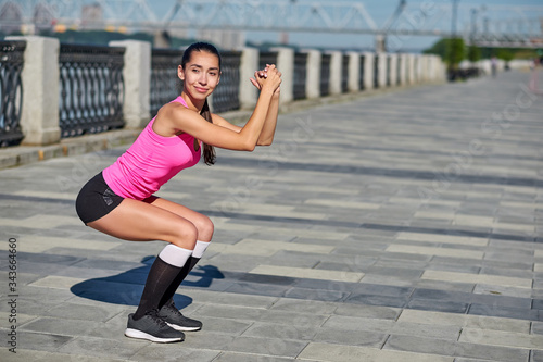 Fitness woman doing stretching on urban city background. Exercises squat or crouch