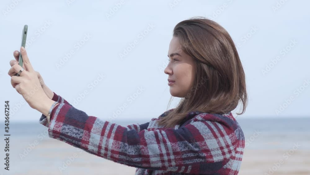 Confident brunette girl taking selfie outdoors. Side view of young brunette woman posing on riverbank and smiling. Joy, lifestyle, millennials, leisure, nature. Confident brunette girl taking selfie outdoors. Side view of young brunette woman posing on riverbank and smiling. Joy, lifestyle, millennials, leisure, nature.