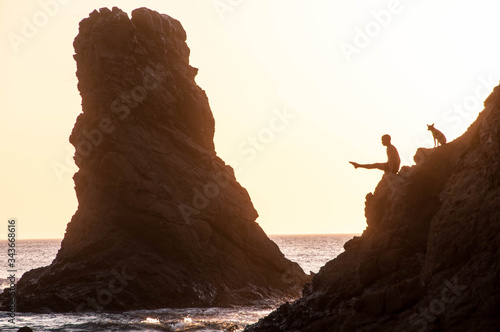 Silhoutte of a man doing handbalance  at the edge of a clif at the beach and his dog photo