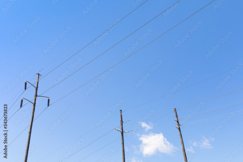 Three electrical power poles side by side, strain insulators, against a blue sky, horizontal aspect Three electrical power poles side by side, strain insulators, against a blue sky, horizontal aspect