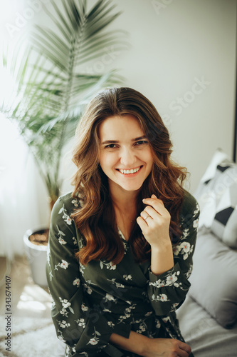 young woman sitting on a sofa in a bright room with a tropical house plant in the background