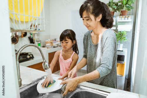 happy mother and daughter washing dishes with detergent on kitchen