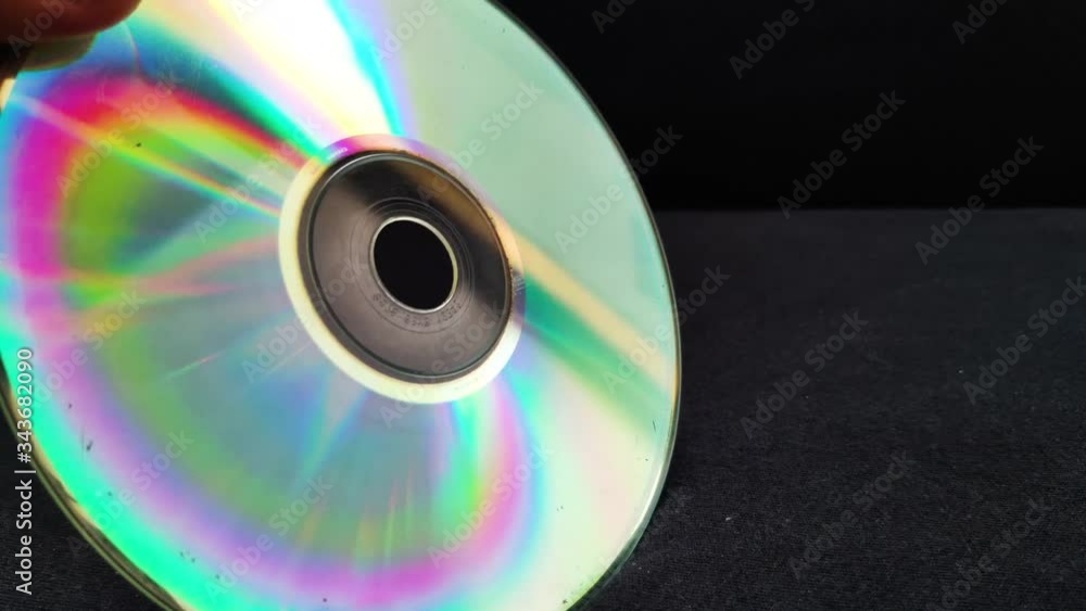 Male hand holds compact disc at different angles to form spectrum on the surface of the disc Male hand holds compact disc at different angles to form spectrum on the surface of the disc