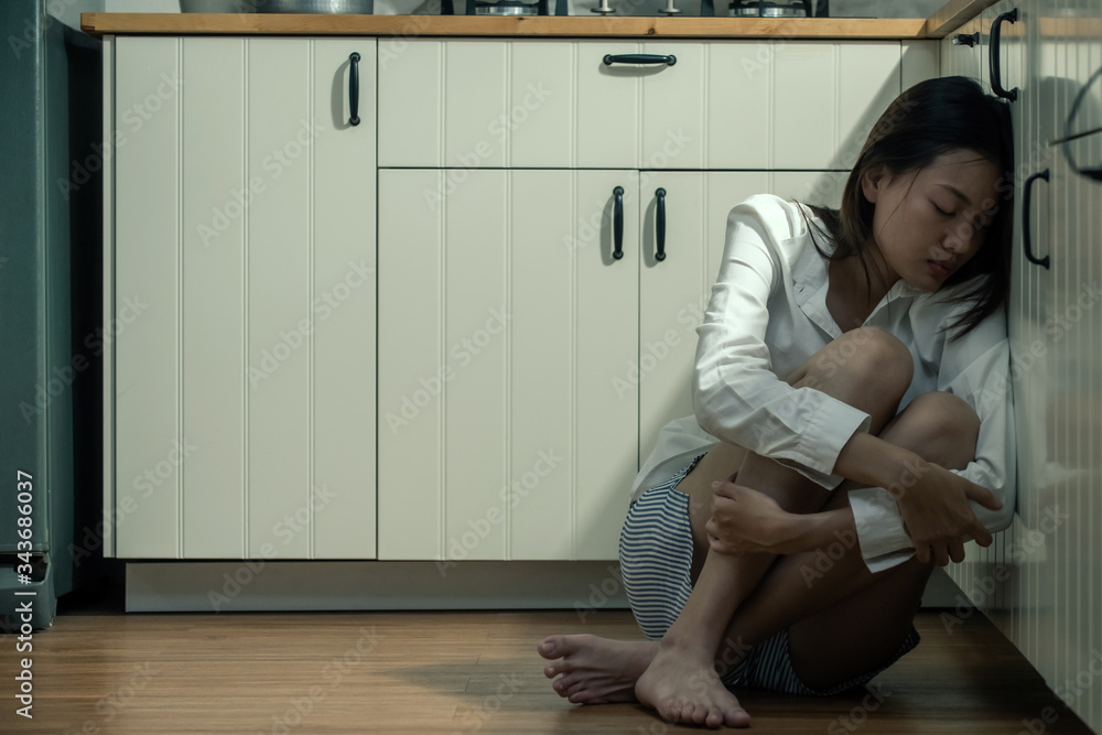 Depressed young beautiful Asian woman sitting on kitchen floor hugging ...