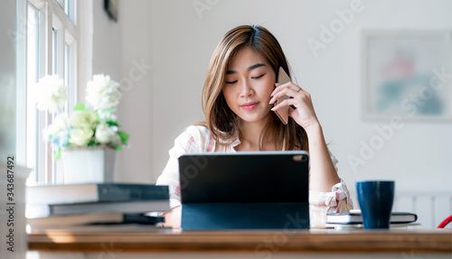 Young asian woman using smartphone and working with laptop at home.