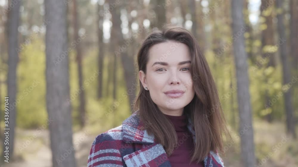 Camera approaching to charming face of gorgeous brunette Caucasian woman posing in forest. Young brown-eyed girl standing in sunlight outdoors. Nature, leisure, joy, lifestyle, beauty. Camera approaching to charming face of gorgeous brunette Caucasian woman posing in forest. Young brown-eyed girl standing in sunlight outdoors. Nature, leisure, joy, lifestyle, beauty.