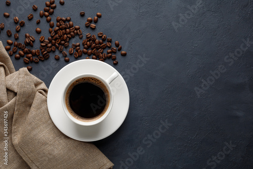 Mug of coffee, napkin and coffee beans on the kitchen table. Black stone background. Top view with copy space.