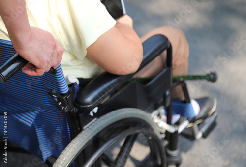 Closeup of man's hand assisting elderly woman in wheelchair in sunny day. 