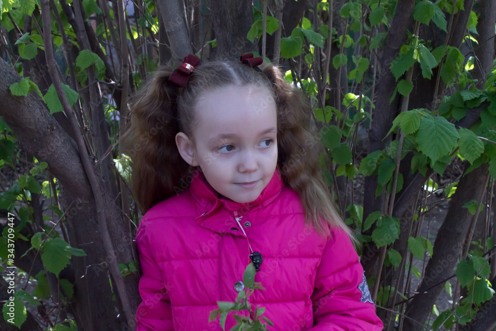 little girl in a pink jacket looks away And smiles in the spring in the garden little girl in a pink jacket looks away And smiles in the spring in the garden