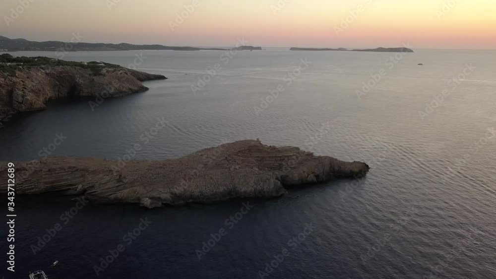 Zoom in on a small peninsula in Ibiza at goldenhour at the top four tourists. In the background the coast and some islands