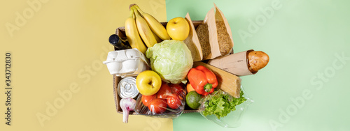 Top view of cardboard box with food products on color green-yellow background. Safe delivery. Banner with copy space.