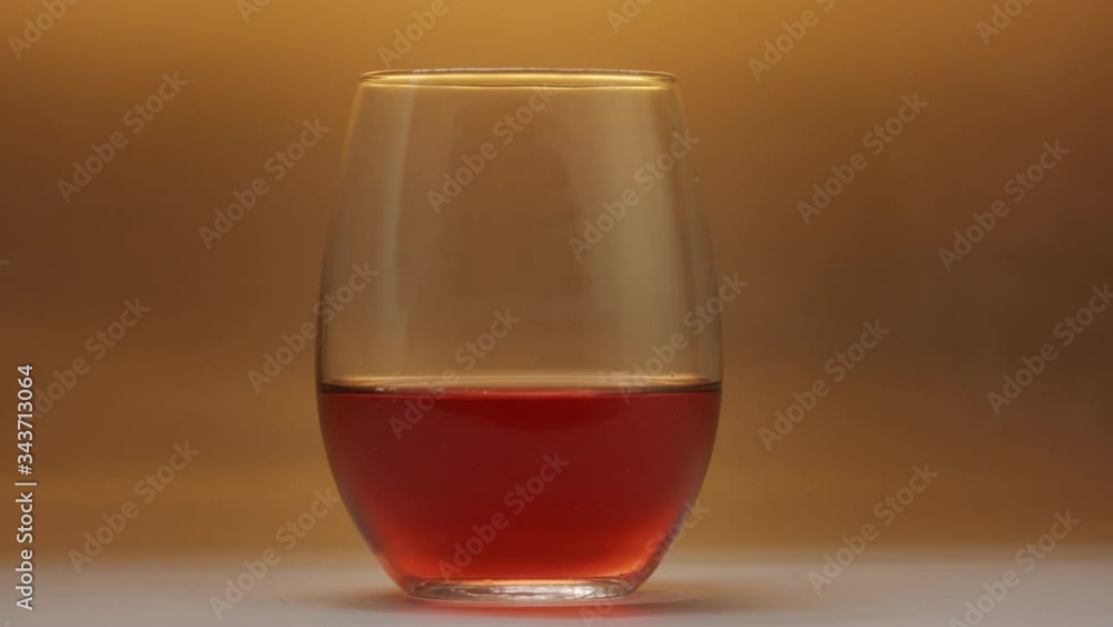 Sparkling wine being poured over half full glass in front of amber background in slow motion. Sparkling wine being poured over half full glass in front of amber background in slow motion.
