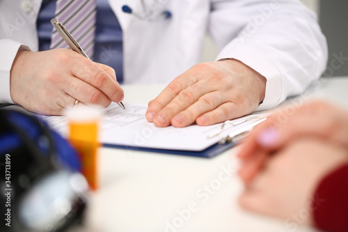 Male doctor hand hold silver pen filling patient history list at clipboard pad. Physical exam er disease prevention ward round visit check 911 prescribe remedy healthy lifestyle concept