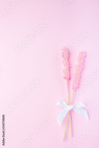 Rock candy on pink paper background decorated with a white bow, vertical, top view, copy space