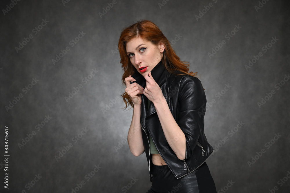 Pretty Model with great makeup posing on a gray background in the studio. Horizontal portrait of a red-haired young woman in a black jacket and green t-shirt. Pretty Model with great makeup posing on a gray background in the studio. Horizontal portrait of a red-haired young woman in a black jacket and green t-shirt.