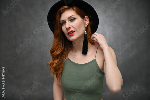Model in a hat with great makeup posing in a green T-shirt in the studio. Portrait on a gray background of a pretty red-haired young woman.
