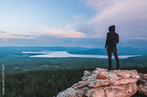 A lonely man in black clothes standing on the rock at the top of Zyuratkul' National Park mountains looking at the valley and lake