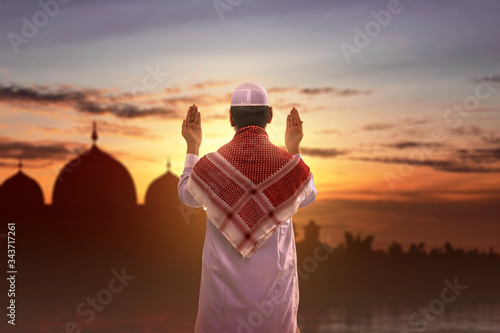 Rear view of Asian Muslim man standing while raised hands and praying