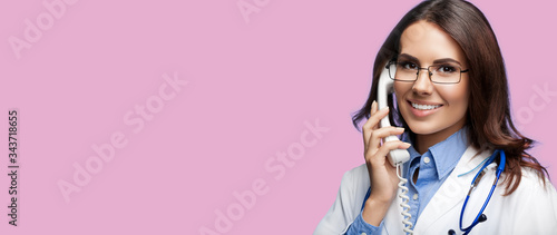 Portrait picture of happy smiling young doctor talking on phone, over pink color background. Copy space for some sign, slogan or advertising text. Medical call center service. photo