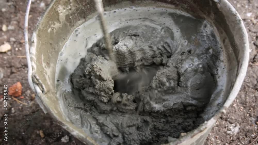 Builder is mixing cement in a bucket with a construction mixer. mixing