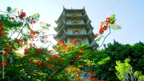 Sun shining through a red blooming flamboyant tree in front of the Buddhist Non Nuoc Pagoda Tower in Da Nang, Vietnam photo