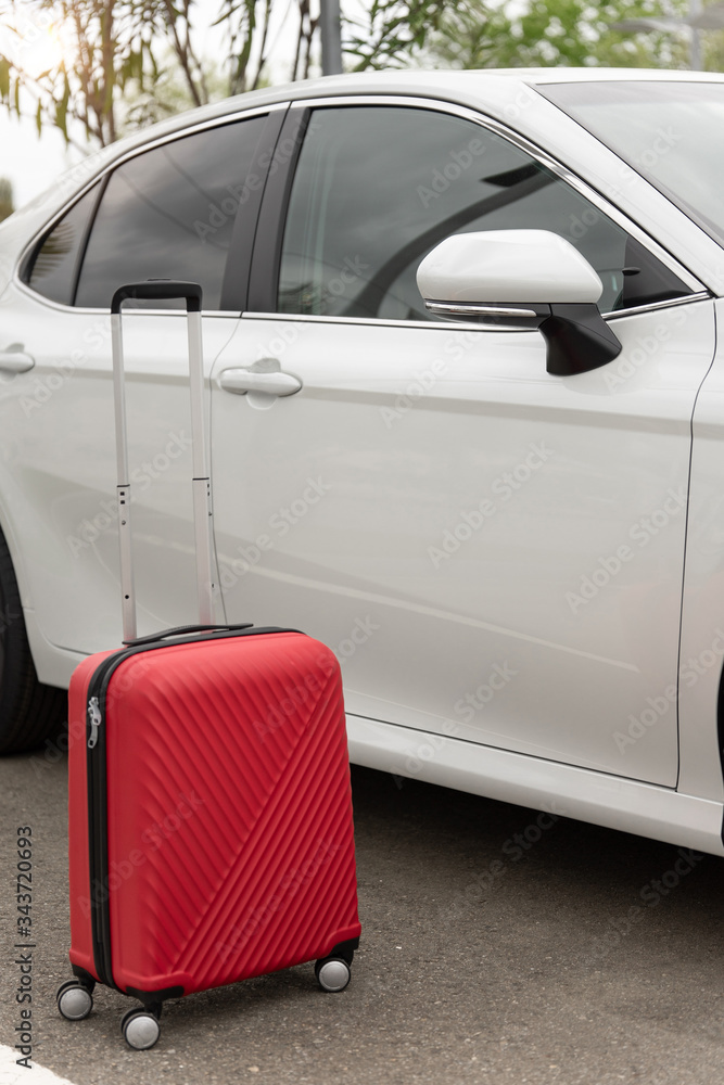 The concept of traveling by car. Transfer. Cardsharing. A red suitcase next to a white car