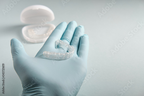 The doctor in gloves holds in his hand a plastic mouthpiece for teeth, on a blue background, a place for an inscription, side view