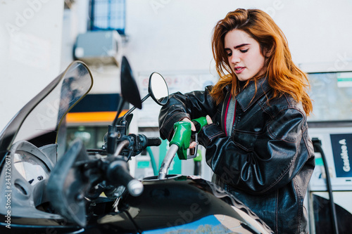 young woman refueling her motorcycle at the gas station, concept of refueling and traveling