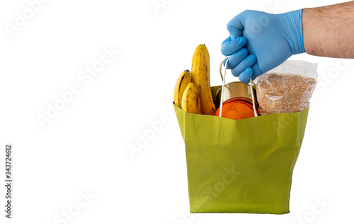 rubber-gloved hand holds out a paper bag of food. delivery during the coronavirus COVID-19 quarantine period.