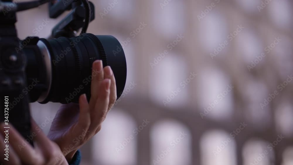 Female filmmaker shifts focus on cine lens on cinema camera with blurry building Female filmmaker shifts focus on cine lens on cinema camera with blurry building