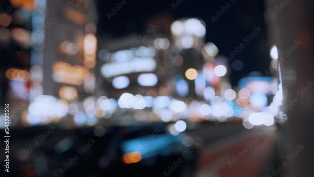 Blurred cars and motorcycle crossing street in the night. Round colorful bokeh shine from car lights in traffic and skyscraper buildings. Blurry asian road at night time. Slow motion. Blurred cars and motorcycle crossing street in the night. Round colorful bokeh shine from car lights in traffic and skyscraper buildings. Blurry asian road at night time. Slow motion.