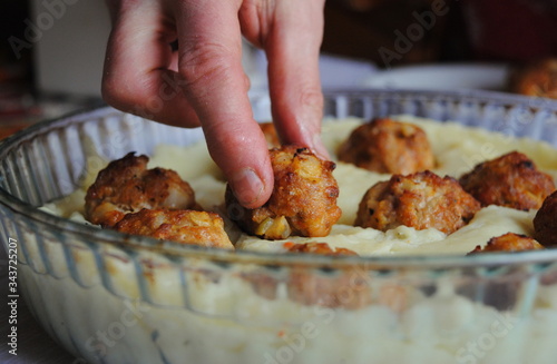 Housewife puts the Meatballs in the Mashed potatoes, preparing for bake. Mashed potatoes casserole recipe.